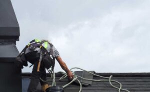 A homeowner on a ladder inspecting shingles on a residential roof in clear weather.